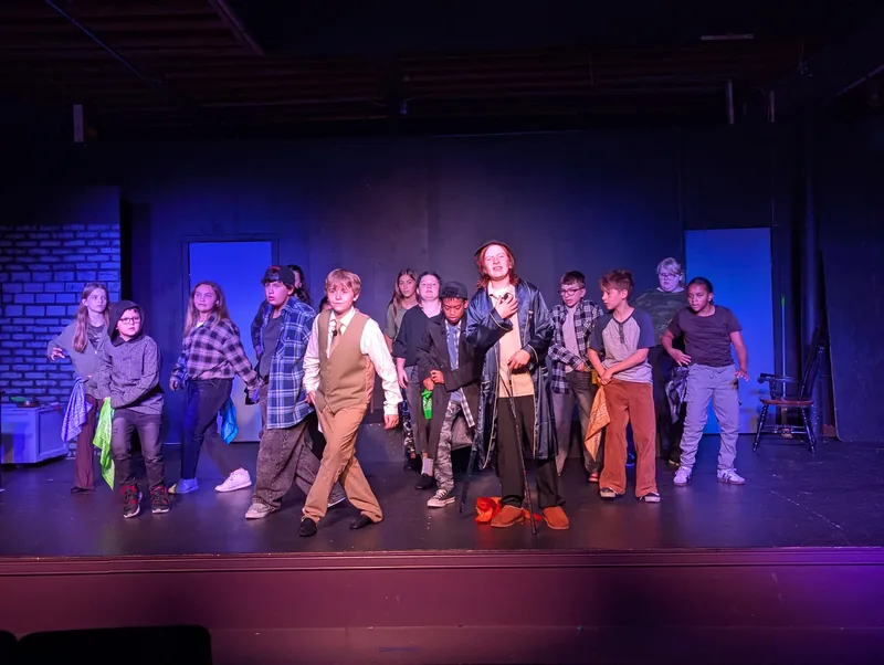 The company of Oliver! The Musical under stage lights