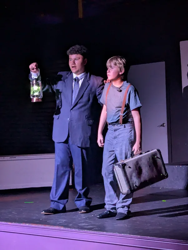 Two students performing a scene with a suitcase in Oliver! The Musical