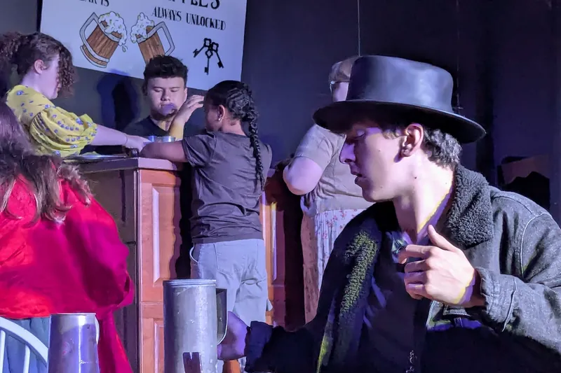 A character in a top hat in a tavern scene from Oliver! The Musical