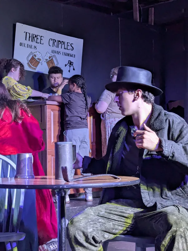 A character in a top hat in a tavern scene from Oliver! The Musical