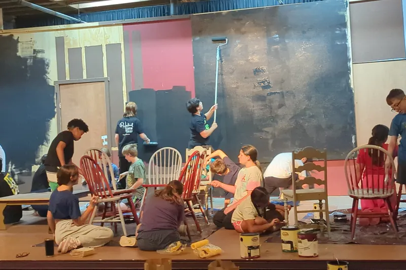Students painting chairs and scenery during build week